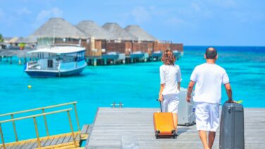A couple arriving at a luxurious Maldives resort dock with luggage, capturing a tropical vacation vibe.